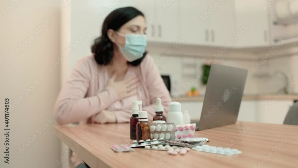 Sick woman in mask talking to doctor online, prescribed medication on table Sick woman in mask talking to doctor online, prescribed medication on table
