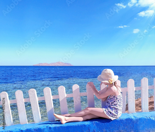 An attractive girl in  straw hat sits on by the sea at sunset. stock photo