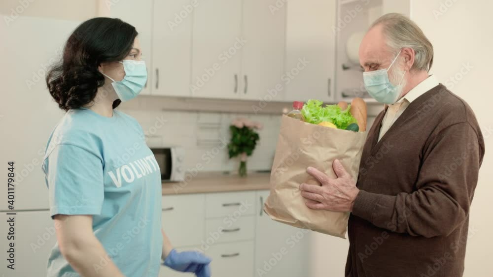Social worker in protective mask giving groceries to aged pensioner, charity Social worker in protective mask giving groceries to aged pensioner, charity