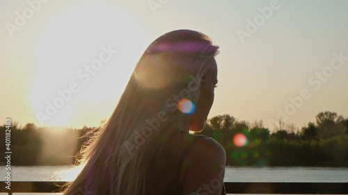 Tilting shot of blond lady in her 30s holding skateboard bekind her back. She is posing and speking to the shooter. photo