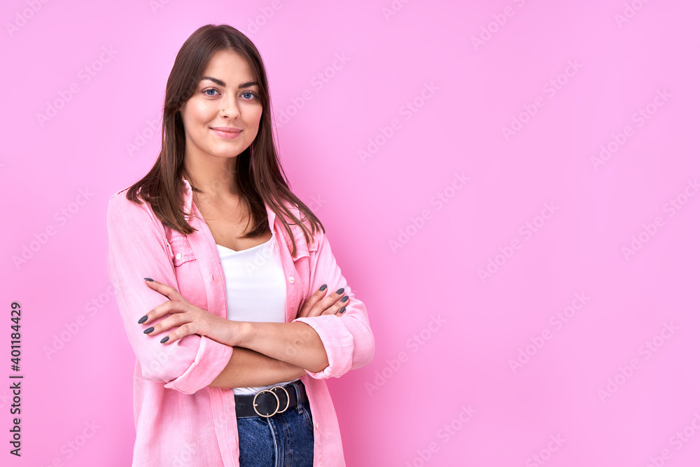 Close Up portrait young brunette woman in pink casual smiling with crossed arms pose and looking at the camera isolated on studio background with copy space Close Up portrait young brunette woman in pink casual smiling with crossed arms pose and looking at the camera isolated on studio background with copy space