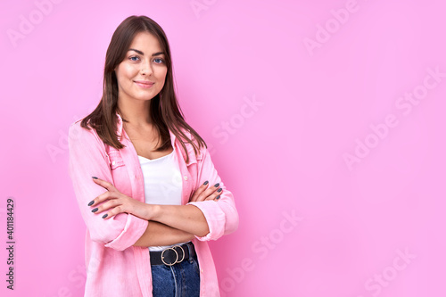 Close Up portrait young brunette woman in pink casual smiling with crossed arms pose and looking at the camera isolated on studio background with copy space