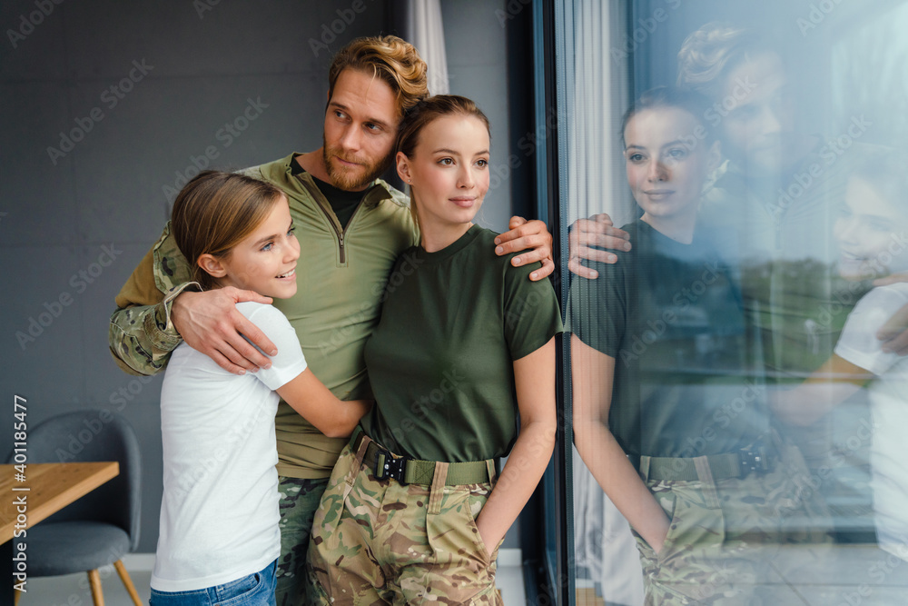 Beautiful happy family hugging while standing near window at home