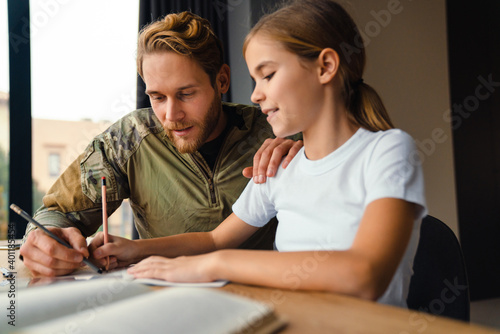 Masculine pleased military man doing homework with her daughter at home