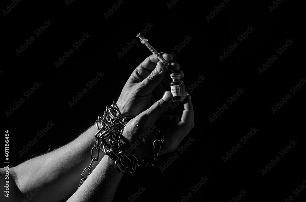 Human hands chained in chains are taking an injection into a syringe from an ampoule with a covid-19 vaccine isolated on a black background