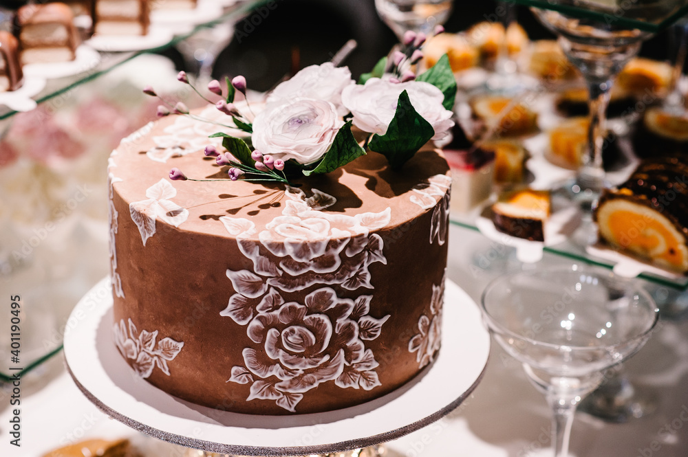 White and brown wedding cake with pink flowers and greens on a festive table and blur background.