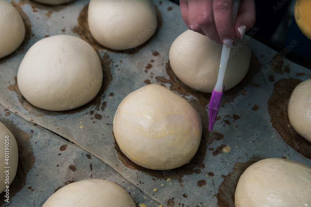 Close-Up of fresh Hamburger Buns, dough. bakery products. production and cooking. Silicone and plastic brush with an egg. Woman hands Close-Up of fresh Hamburger Buns, dough. bakery products. production and cooking. Silicone and plastic brush with an egg. Woman hands