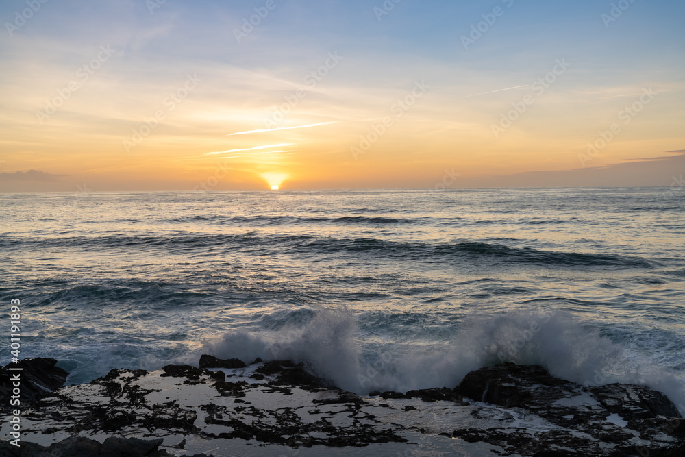 large waves crash onto rocky shore with tidal pools at sunset