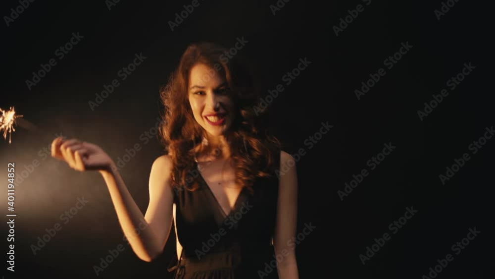 Positive young woman with sparkler talking on black background Positive young woman with sparkler talking on black background