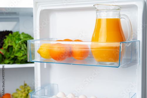 Glass pitcher of orange juice and fruits on fridge shelf