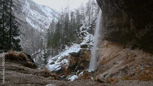 Waterfall Pericnik in Slovenia. Water plunges in waterfall base. Famous path under waterfall. Snow covering nature in winter season in Alps mountains. Static shot, real time, wide angle