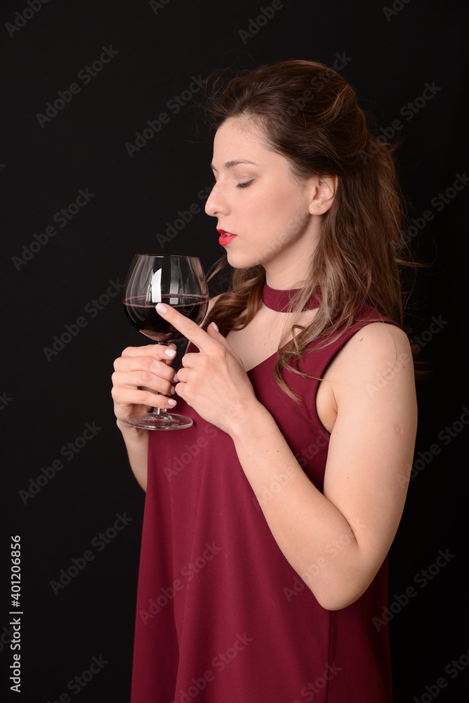 girl with red lips in a Marsala dress holding a glass of red wine in her hands on a black background girl with red lips in a Marsala dress holding a glass of red wine in her hands on a black background