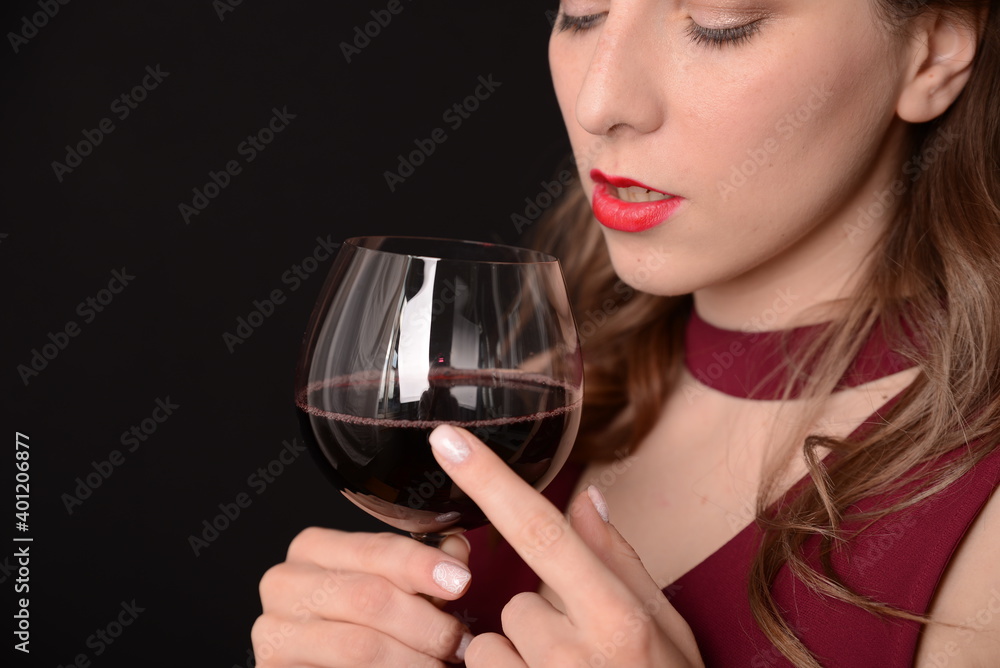 girl with red lips in a Marsala dress holding a glass of red wine in her hands on a black background girl with red lips in a Marsala dress holding a glass of red wine in her hands on a black background