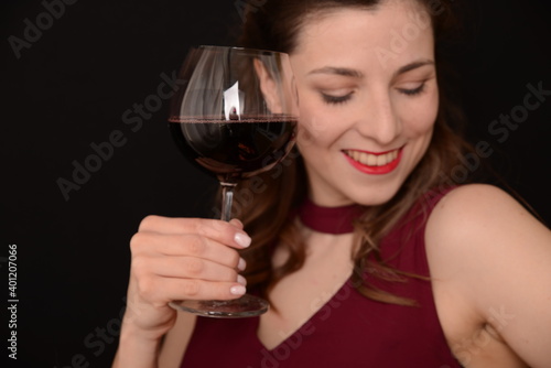 girl with red lips in a Marsala dress holding a glass of red wine in her hands on a black background