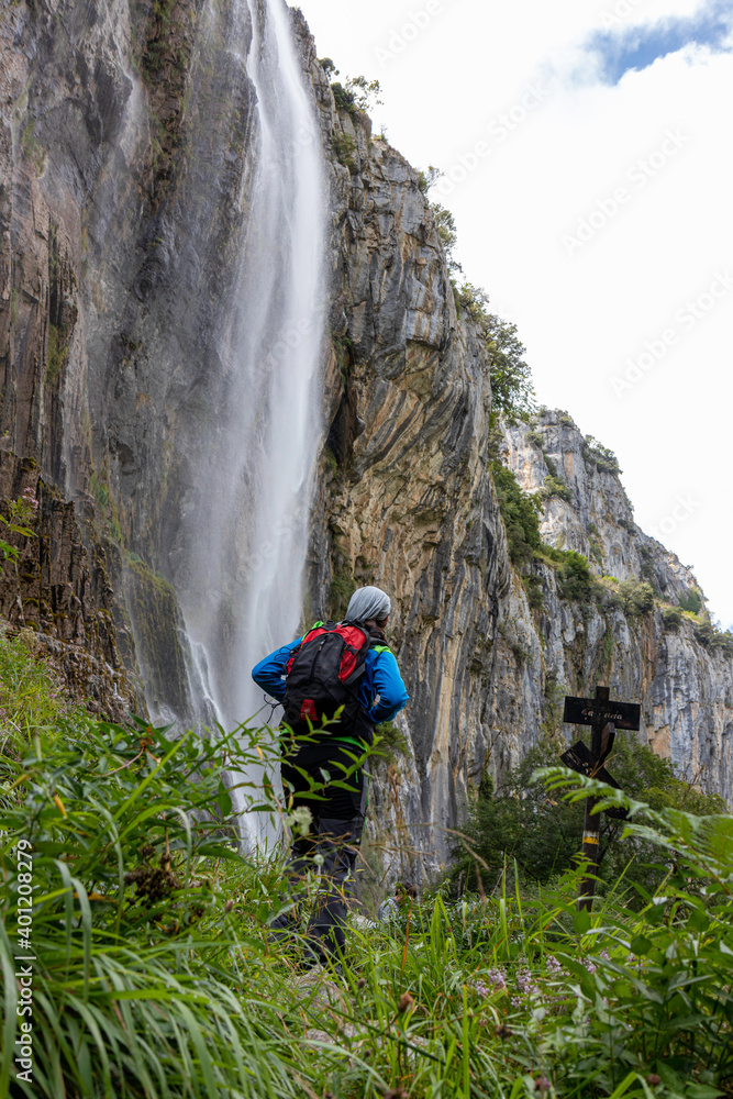 Hombre joven senderista junto a una cascada en el nacimiento del rio Asón en Cantábria Hombre joven senderista junto a una cascada en el nacimiento del rio Asón en Cantábria