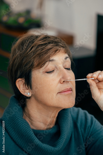 Portrait Senior woman doing a self test for COVID-19 at home with Antigen kit. Introducing nasal swab test for possible infection of Coronavirus. Medicine and health-related services online.