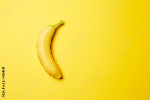 Single fresh raw clean isolated one alone vertically oriented yellow banana on the bright solid yellow fond background