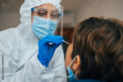 Close up of female health Professional in PPE introducing a nasal swab to a senior female patient at her house. Rapid Antigen Test kit to analyze nasal culture sampling while coronavirus Pandemic. photo