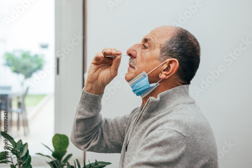 Senior man sitting, self test for COVID-19 at home with Antigen test kit. Coronavirus nasal swab test for infection. Medicine and health-related services online. photo