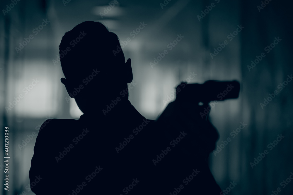 Silhouette of a man with a gun in a dark corridor, close-up.