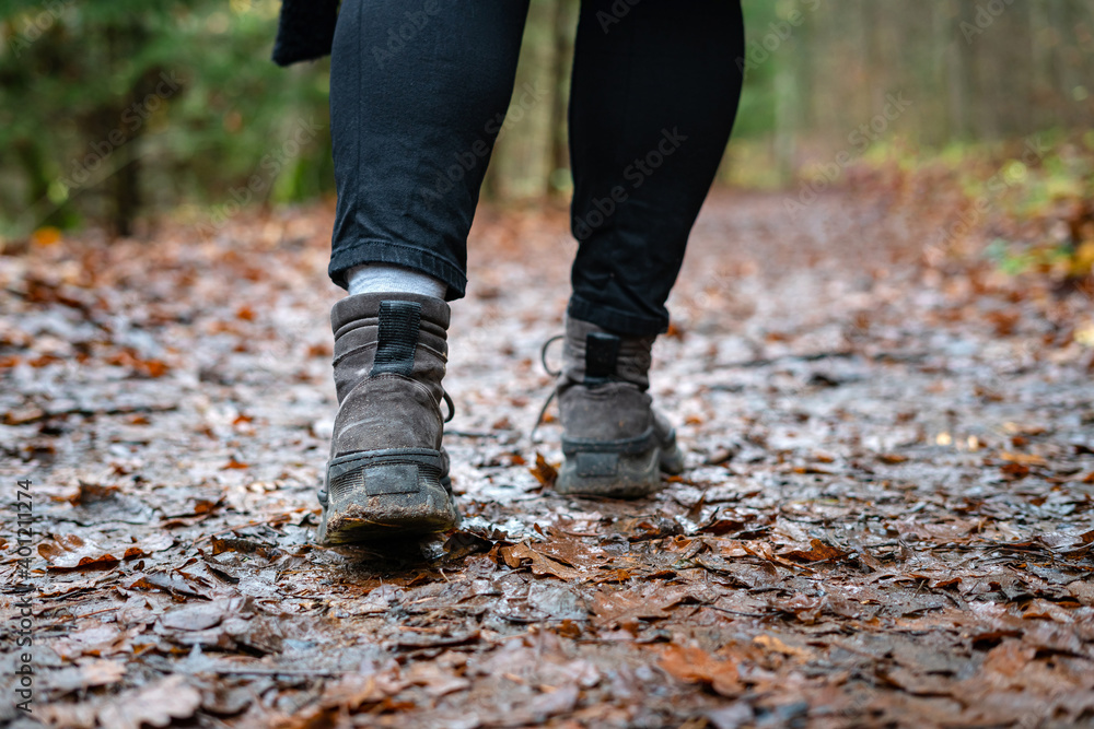 Close up of hiker walking down the wet forest path. Person with dirty hiking shoes on the footpath outdoors. Close up of hiker walking down the wet forest path. Person with dirty hiking shoes on the footpath outdoors.