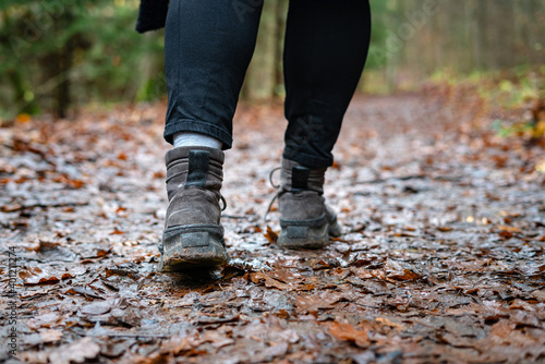 Close up of hiker walking down the wet forest path. Person with dirty hiking shoes on the footpath outdoors.