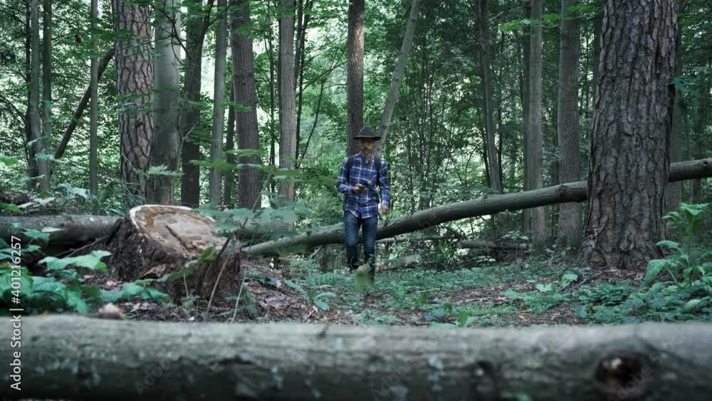 Stylish young man in felt hat and plaid shirt with leather backpack walking in forest and navigate using smartphone. Escape into the wild. Adventure vibes and wanderlust. Stylish young man in felt hat and plaid shirt with leather backpack walking in forest and navigate using smartphone. Escape into the wild. Adventure vibes and wanderlust.
