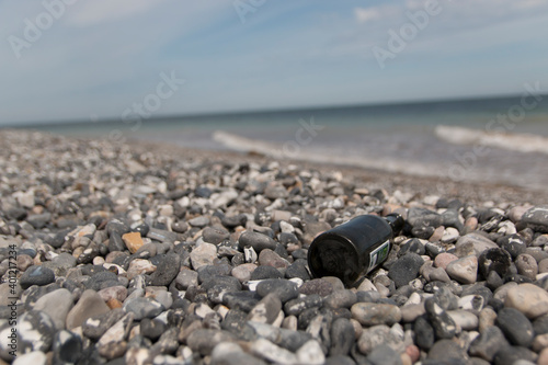 A green beer bottle lies in the rocks on a beach, the sea and waves are seen in the background