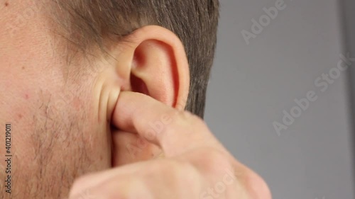 man picks his left ear with his index finger, loud noise or itch, personal hygiene, close-up, gray background