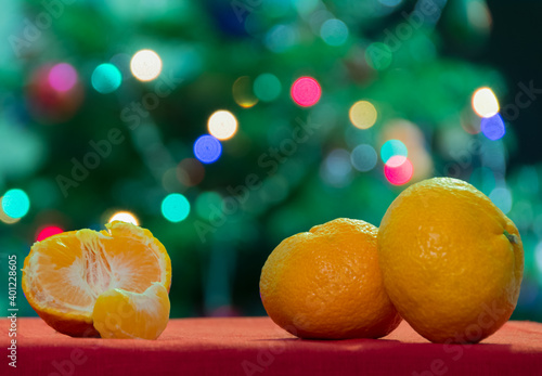 Christmas concept with Tangerines on a table with a red tablecloth, in the background Boke from garland.