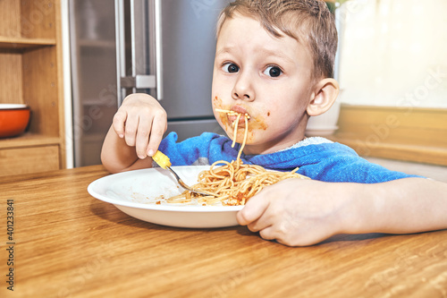 Obraz na plátně Lovely boy kid with large eyes eats sloppy delicious pasta with yellow baby fork