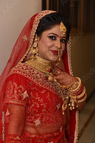 Cute Indian bride posing with victory sign for photograph. She is wearing traditional red color indian dress 