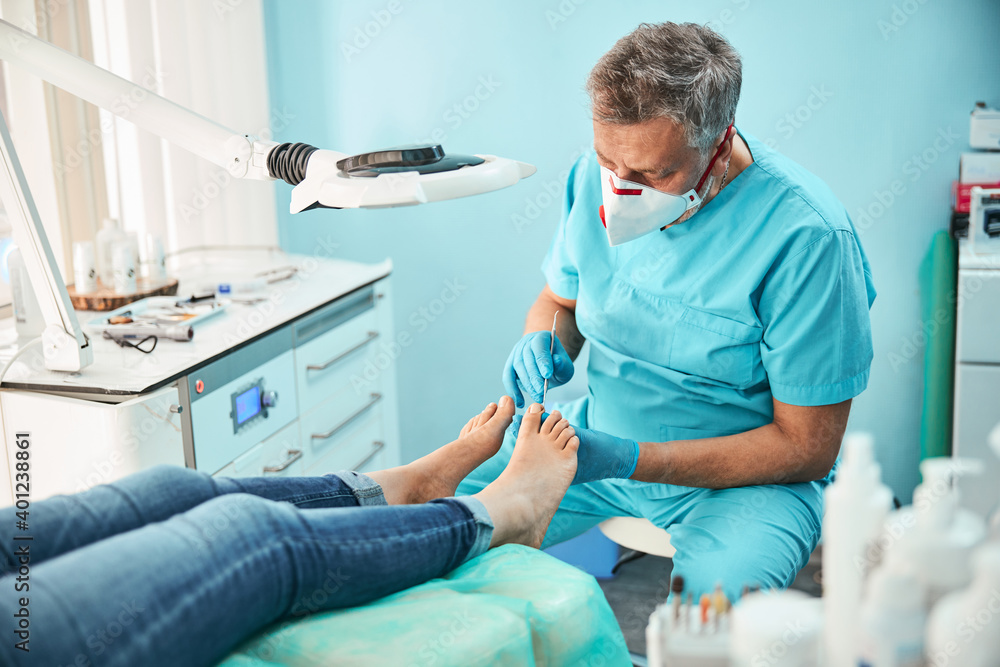 Obraz premium Unrecognized female patient sitting on the medical chair at the pedicure procedure in medicine center