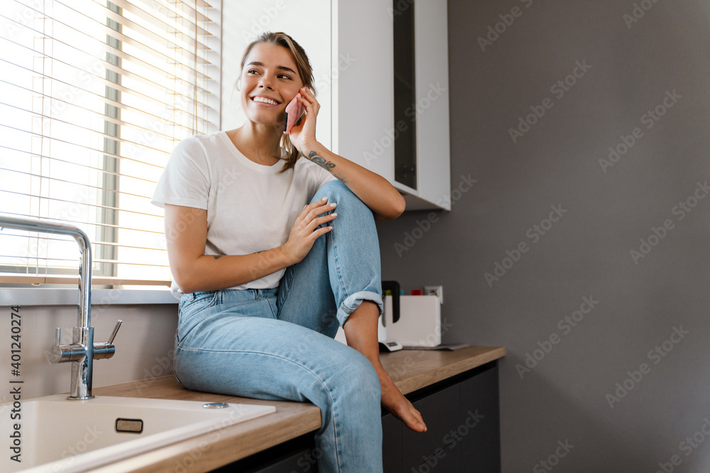 Beautiful joyful girl smiling and talking on mobile phone while sitting Beautiful joyful girl smiling and talking on mobile phone while sitting