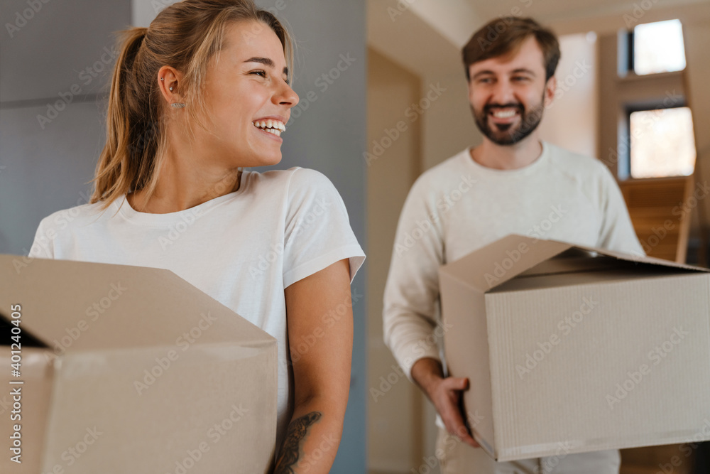 Beautiful couple smiling and carrying cardboard boxes in new apartment Beautiful couple smiling and carrying cardboard boxes in new apartment