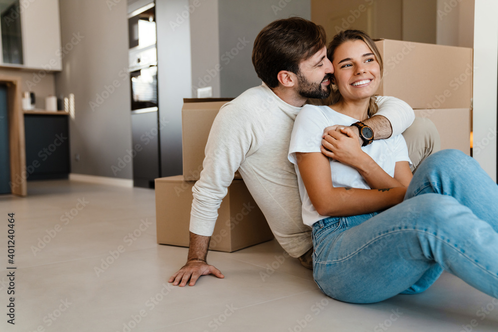 Beautiful couple hugging while sitting with boxes in new apartment Beautiful couple hugging while sitting with boxes in new apartment