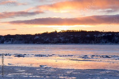 Sunrise view of the St. Lawrence River partly covered in ice with a scattering of houses on the south shore cliff in the background, Quebec City, Quebec, Canada