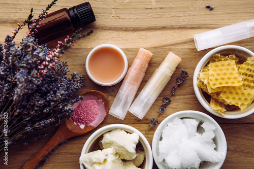 Ingredients for homemade lip balm: shea butter, essential oil, mineral color powder, beeswax, coconut oil. Homemade lip balm lipstick mixture with ingredients scattered around. photo