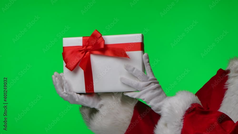Side view of Santa Claus in white gloves and a red suit twirls a gift box in his hands. Isolated on a green screen in a studio. Chroma key. Close up. Slow motion. Side view of Santa Claus in white gloves and a red suit twirls a gift box in his hands. Isolated on a green screen in a studio. Chroma key. Close up. Slow motion.