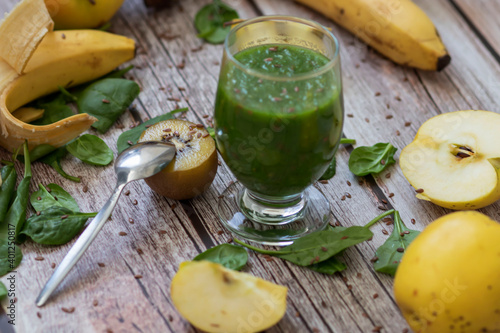 
A glass of kiwi, spinach and apple smoothie. Health drink. Apples, flax seeds, spinach, kiwi, bananas lie nearby.