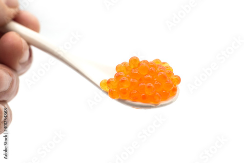 Closeup of trout eggs in a white ceramic spoon on white background