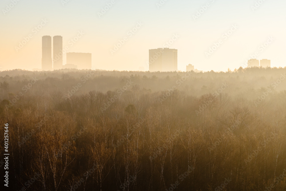 urban park and high-rise buildings on horizon lit by yellow sunrise sun in cold winter morning in Moscow city