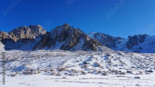 High rocks covered with snow. The Tuyuk Su Glacier. The view from the drone to the tops of the peaks. Completely surrounded by winter mountains. blue clear sky and bright sun. Shadows from mountains