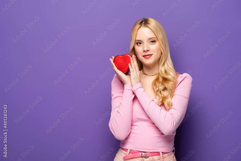 blonde young woman holding red heart shaped box on purple background. blonde young woman holding red heart shaped box on purple background.