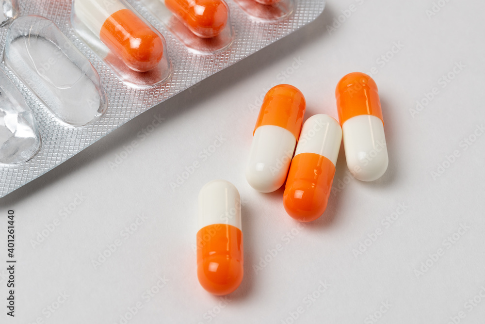 Macro photo of white and orange medical capsules on a white background. Medications pills or vitamins in a blister close up Macro photo of white and orange medical capsules on a white background. Medications pills or vitamins in a blister close up