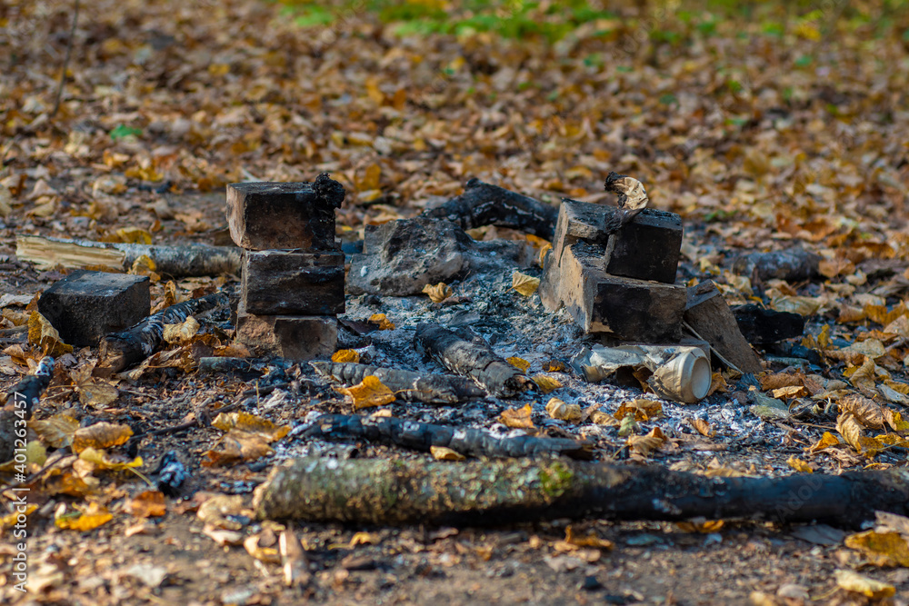 Remains of a burnt campfire in the forest. Charcoal and burnt branches at a picnic site in the park among autumn leaves. Remains of a burnt campfire in the forest. Charcoal and burnt branches at a picnic site in the park among autumn leaves.