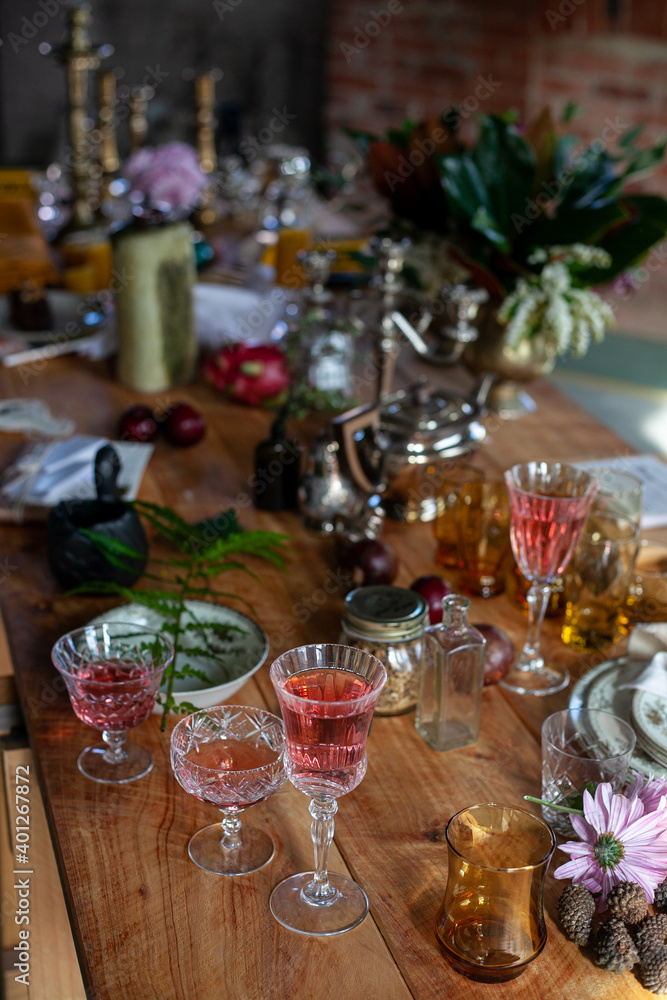 a variety of crystal glasses with rose wine, plates, candlesticks and other vintage staff in a mess on a wooden table