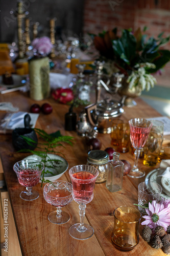 a variety of crystal glasses with rose wine  plates  candlesticks and other vintage staff in a mess on a wooden table