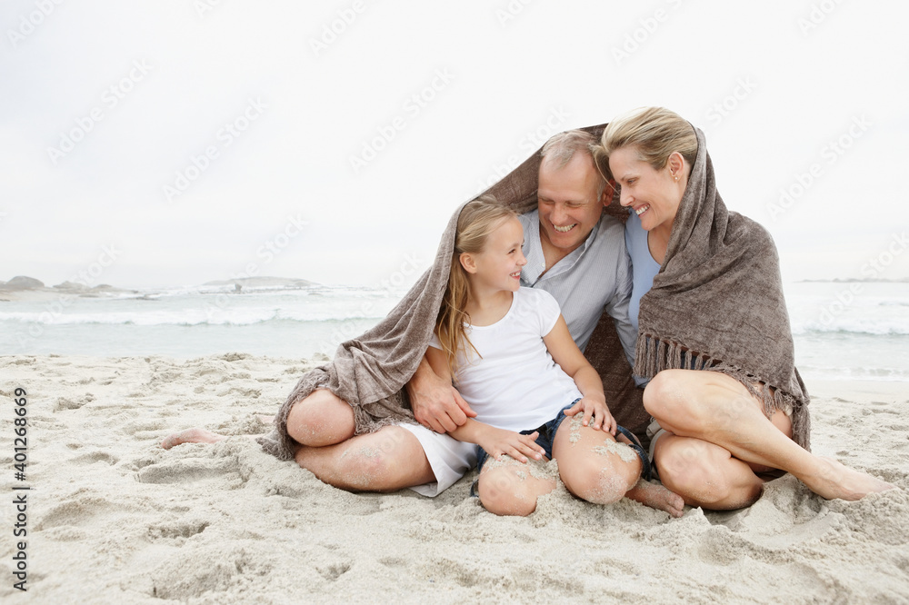 Smiling parents with daughter (10-11) on coastline covered by blanket Smiling parents with daughter (10-11) on coastline covered by blanket