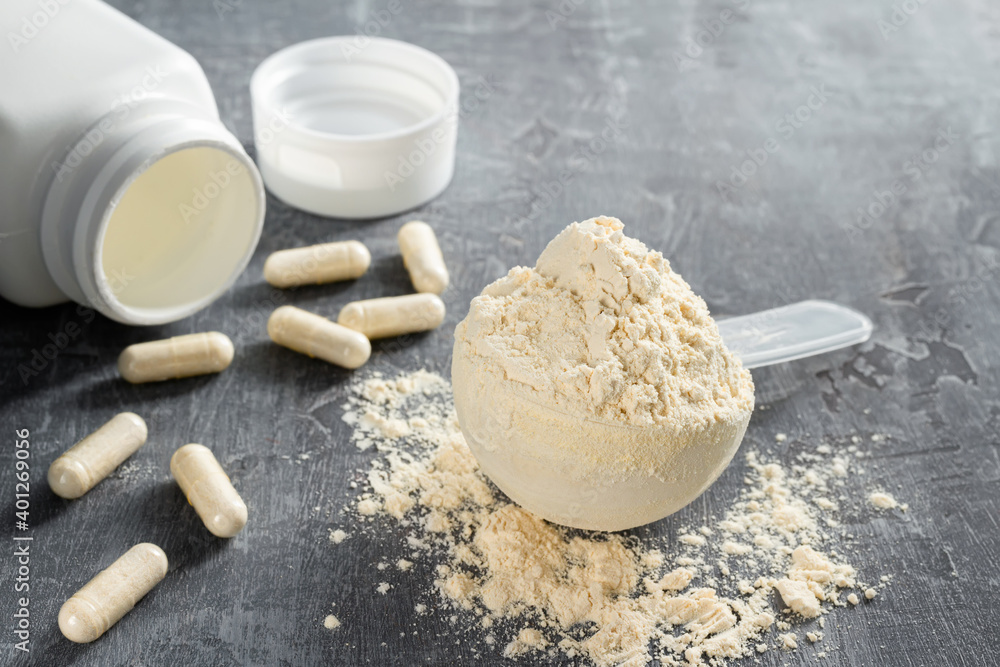 Scoop of whey or soy protein isolate, white capsules of bcaa, beta-alanine and taurine amino acids, creatine, bodybuilding food supplements on stone background Scoop of whey or soy protein isolate, white capsules of bcaa, beta-alanine and taurine amino acids, creatine, bodybuilding food supplements on stone background